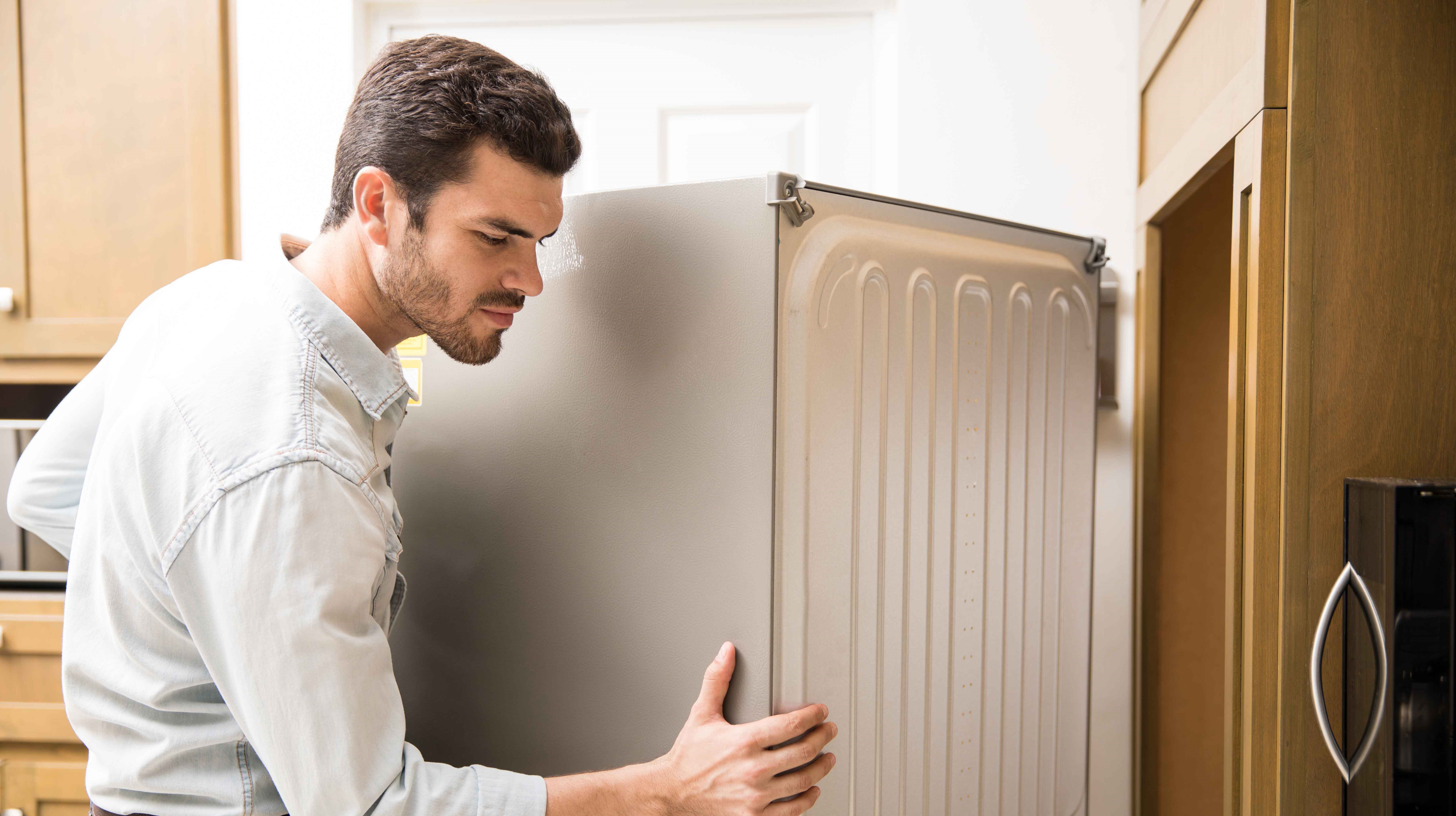 young man working as electrician exposing back fridge check repair it